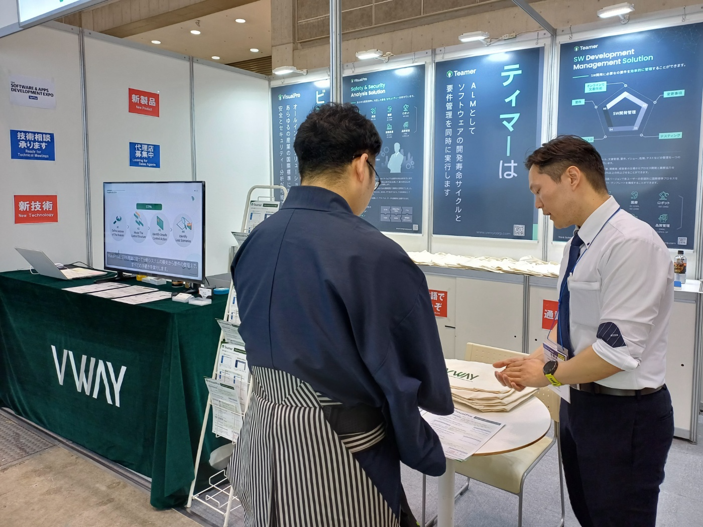 Japan IT Week 2024 Spring 브이웨이 부스에서 방문객에게 VisualPro 의 STPA 4단계(분석 목적 정의·컨트롤 스트럭처 모델링·UCA 식별·손실 시나리오 식별)를 설명하는 모습
