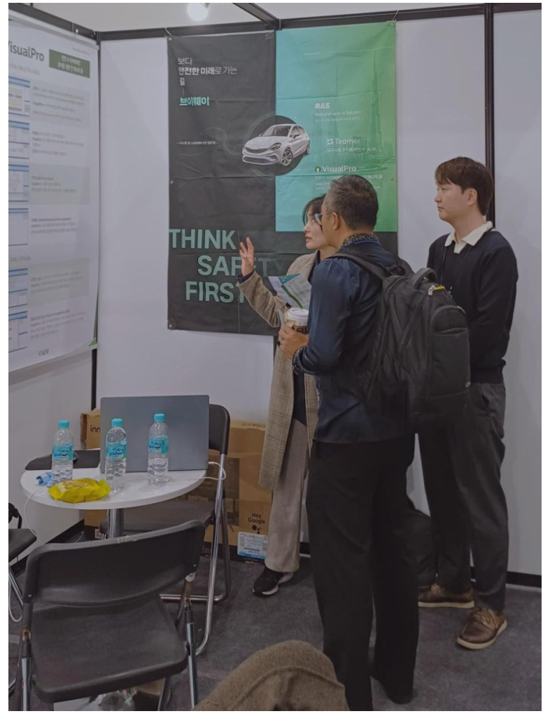 SEDEX 2025 브이웨이 부스 안에서 THINK SAFETY FIRST 배너를 배경으로 방문객과 이야기하는 사진 2장