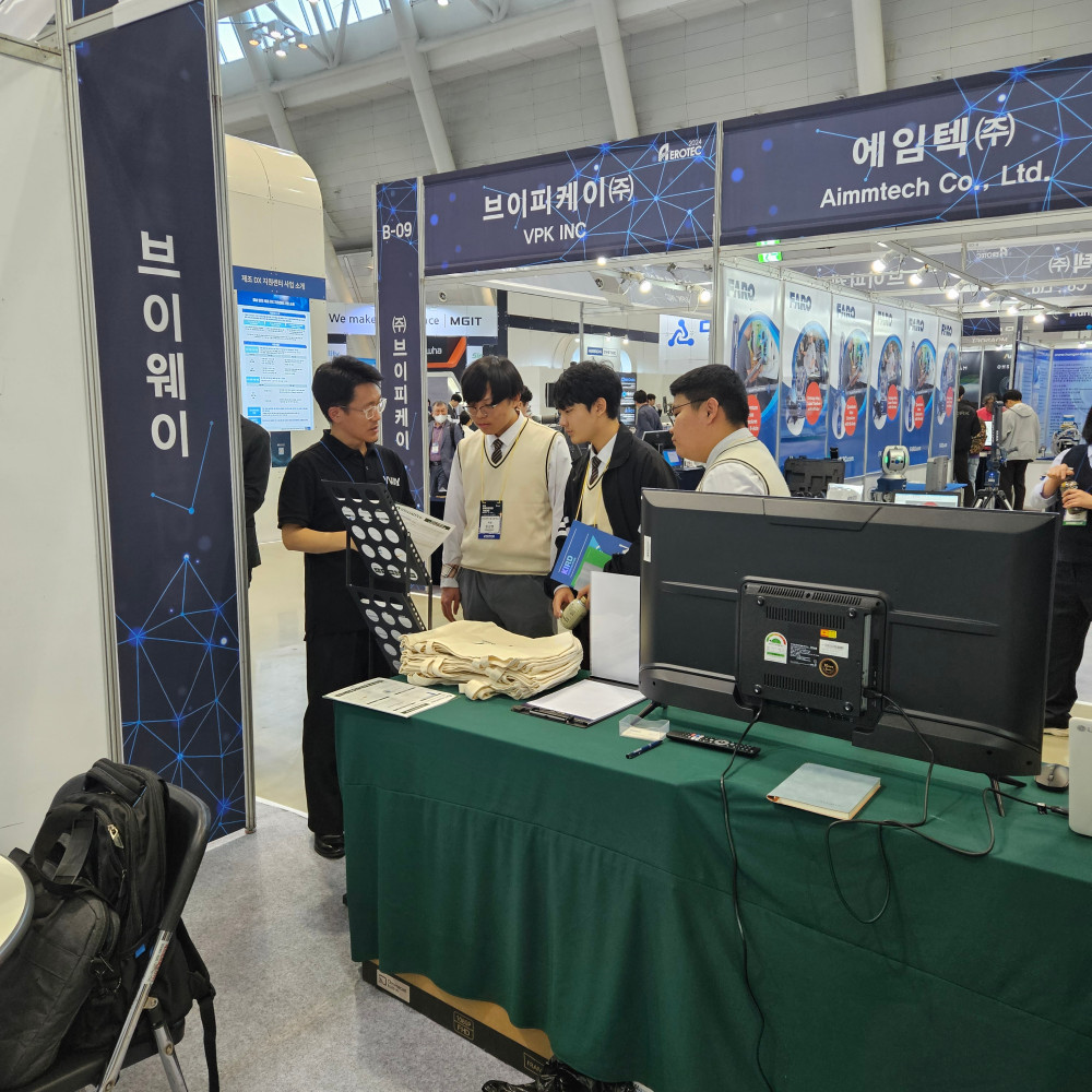 AEROTEC 2024 브이웨이 부스에서 방문객들에게 자료를 설명하는 모습 — 옆에 '브이웨이' 세로 배너